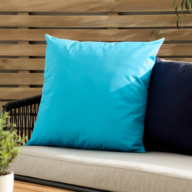 Plain Printed Polyester Cushion in aqua, square with a smooth unpatterned finish, shown on an outdoor sofa beside a navy cushion against a wooden slatted wall.
