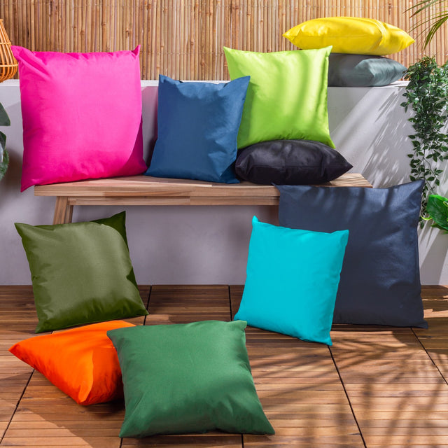 Plain Printed Polyester Cushion in lime green, square scatter cushion shown among an assorted colourful cushion display on a wooden bench and deck outdoors.