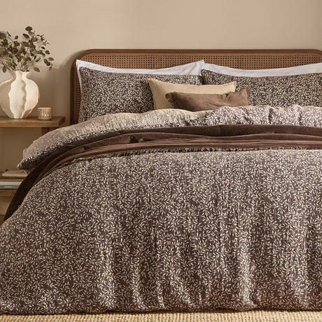 Perrie Leaf Cotton Ditsy Duvet Cover Set in chocolate brown with cream leaf print, styled on a bed with matching pillowcases, brown cushions and a rattan headboard.