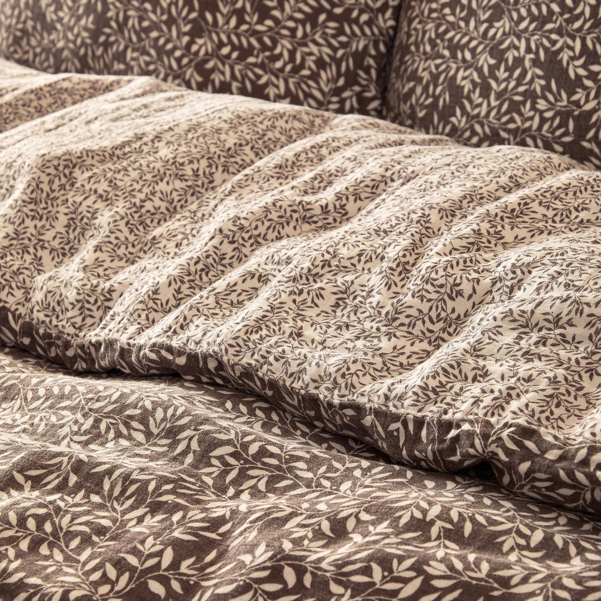 Close-up of the Perrie Leaf Cotton Ditsy Duvet Cover Set in chocolate brown, showing crinkled cotton texture with a small cream leaf print and reverse-side pattern.