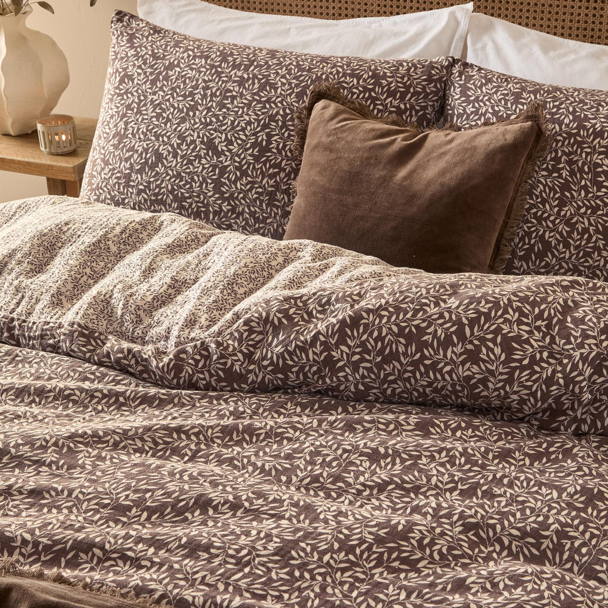 Perrie Leaf Cotton Ditsy Duvet Cover Set in chocolate brown with cream leaf print, shown on a bed with matching pillowcases and a brown velvet cushion.
