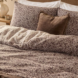 Perrie Leaf Cotton Ditsy Duvet Cover Set in chocolate brown with cream leaf print, shown on a bed with matching pillowcases and a brown velvet cushion.