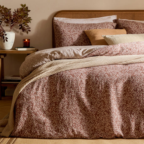 Perrie Leaf Cotton Ditsy Duvet Cover Set in cinnamon, styled on a bed with matching pillowcases, cream leaf print, and layered cushions in a warm-toned bedroom setting.