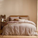Perrie Leaf Cotton Ditsy Duvet Cover Set in Cinnamon, dressed on a bed with matching pillowcases and layered cushions in a warm-toned bedroom setting with a rattan headboard.