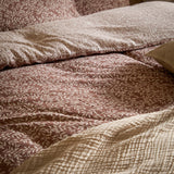 Perrie Leaf Cotton Ditsy Duvet Cover Set in Cinnamon, cream sprig print on a warm brown ground, shown with a textured cream quilted throw and coordinating pillowcases on a bed.