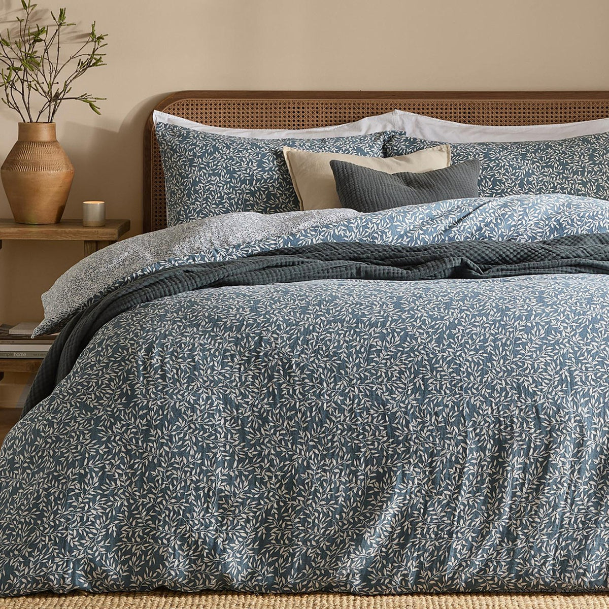 Perrie Leaf Cotton Ditsy Duvet Cover Set in denim blue, styled on a bed with matching pillowcases, a rattan headboard, and layered cushions in a bedroom setting.