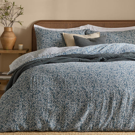 Perrie Leaf Cotton Ditsy Duvet Cover Set in denim blue, styled on a bed with matching pillowcases, a rattan headboard, and layered cushions in a bedroom setting.