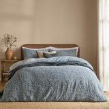 Perrie Leaf Cotton Ditsy Duvet Cover Set in denim blue on a bed, styled with matching pillowcases, cream and grey cushions, and a knitted throw in a warm-toned bedroom.