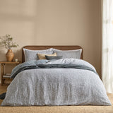Perrie Leaf Cotton Ditsy Duvet Cover Set in denim blue with cream leaf-and-stem print, styled on a bed with matching pillowcases and layered cushions in a neutral bedroom setting.