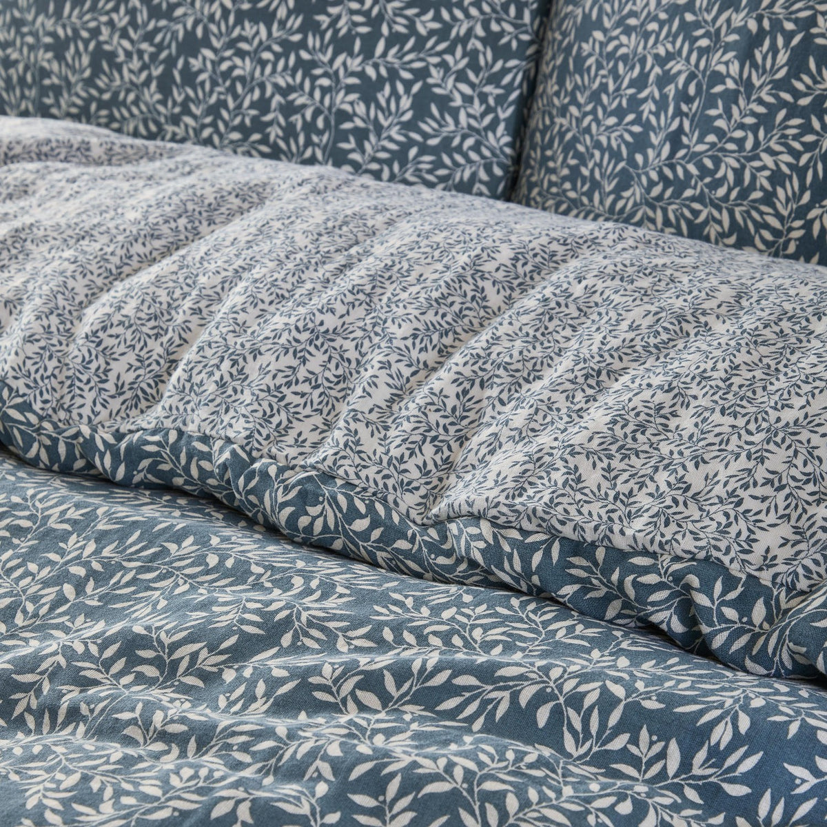 Perrie Leaf Cotton Ditsy Duvet Cover Set in Denim, close-up of crinkled cotton bedding with a small-scale cream leaf print on a blue ground, reverse side shown in plain denim blue.