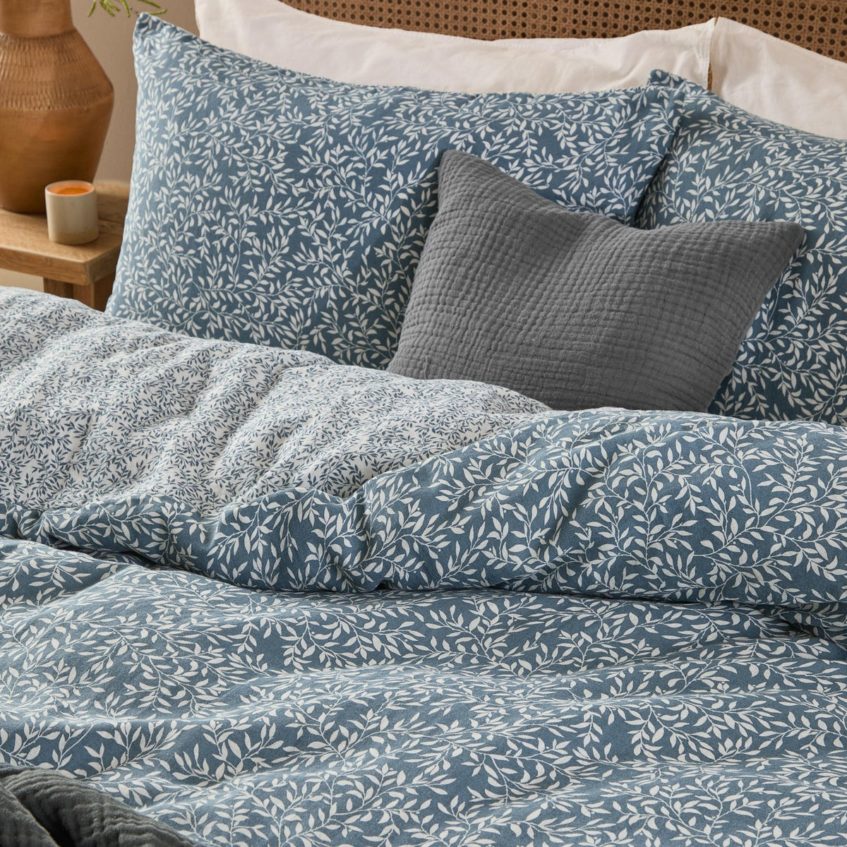 Perrie Leaf Cotton Ditsy Duvet Cover Set in denim blue with cream leaf-and-stem print, shown on a bed with matching pillowcases and a grey textured cushion.