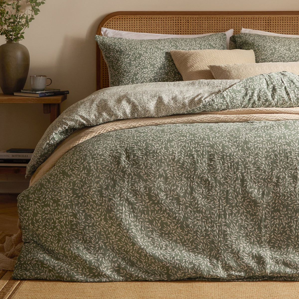 Perrie Leaf Cotton Ditsy Duvet Cover Set in Forest green, shown on a bed with matching pillowcases and layered cushions in a bedroom setting with a rattan headboard.