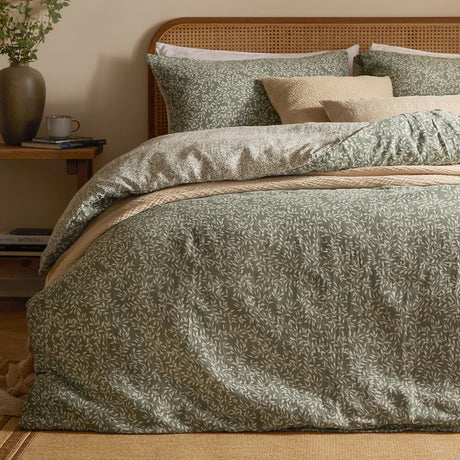 Perrie Leaf Cotton Ditsy Duvet Cover Set in Forest green, shown on a bed with matching pillowcases and layered cushions in a bedroom setting with a rattan headboard.