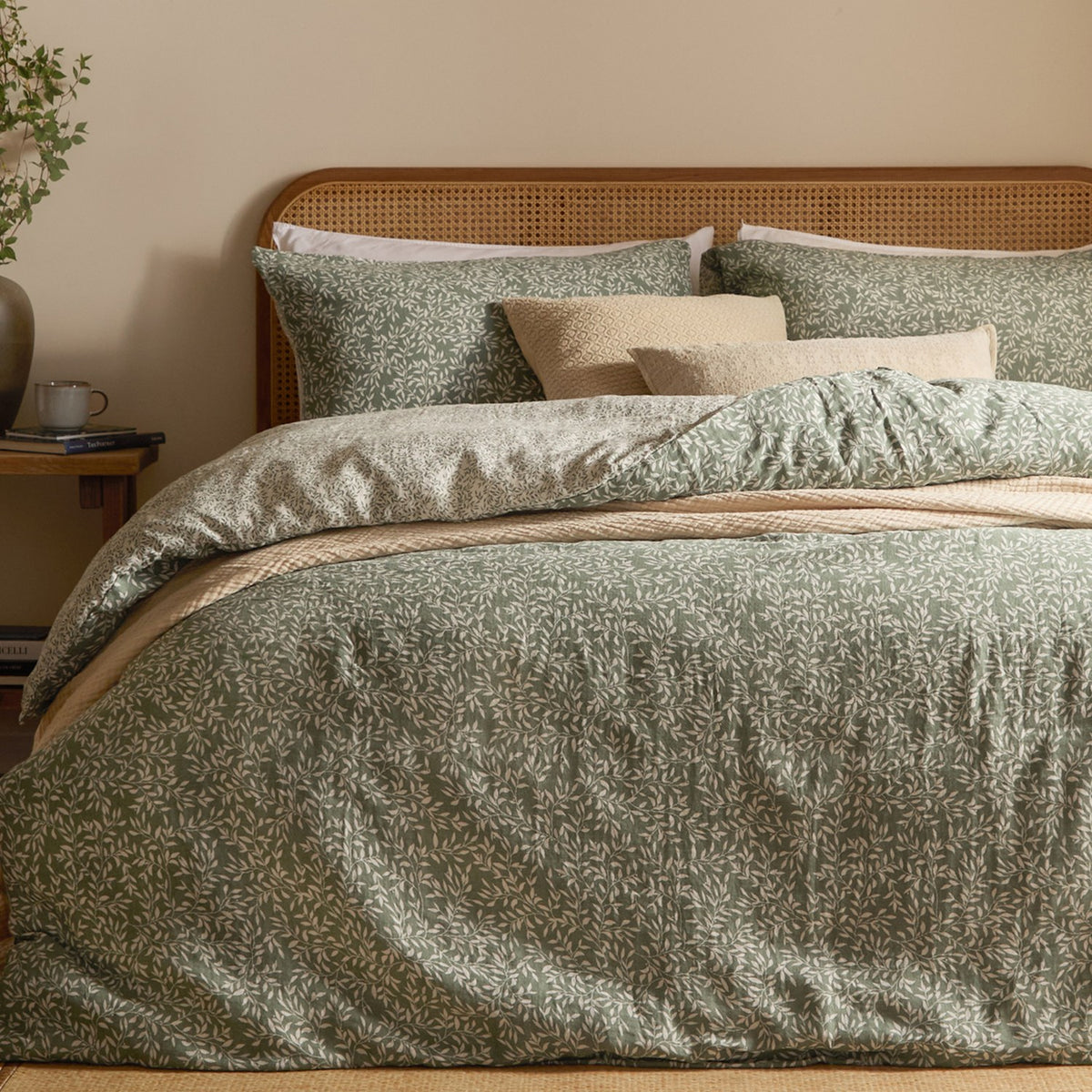 Perrie Leaf Cotton Ditsy Duvet Cover Set in Forest on a bed with cane headboard, showing green ditsy leaf print cotton duvet and matching pillowcases with neutral cushions.