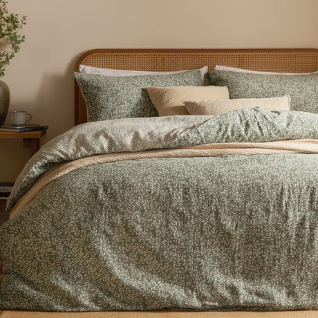 Perrie Leaf Cotton Ditsy Duvet Cover Set in Forest on a bed with cane headboard, showing green ditsy leaf print cotton duvet and matching pillowcases with neutral cushions.
