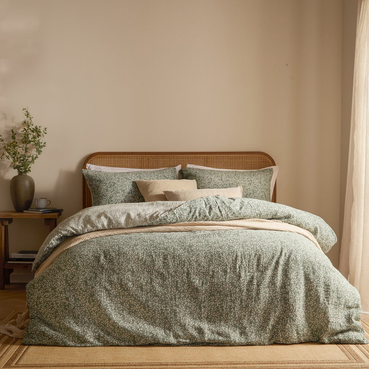 Perrie Leaf Cotton Ditsy Duvet Cover Set in Forest green, styled on a bed with matching pillowcases and cream cushions against a rattan headboard.