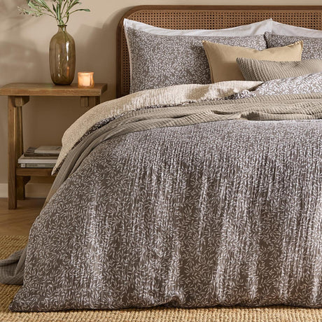 Perrie Leaf Cotton Ditsy Duvet Cover Set in mole, a crinkled cotton muslin with a white leaf print, styled on a bed with cane headboard and layered cushions.