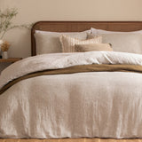Perrie Leaf Cotton Ditsy Duvet Cover Set in Natural, styled on a bed with a rattan headboard, layered pillows, and a mustard textured throw in a bedroom setting.