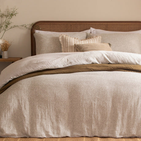 Perrie Leaf Cotton Ditsy Duvet Cover Set in Natural, styled on a bed with a rattan headboard, layered pillows, and a mustard textured throw in a bedroom setting.