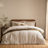 Perrie Leaf Cotton Ditsy Duvet Cover Set in natural, styled on a bed with cane headboard, layered with striped and textured cushions and an olive throw in a neutral bedroom setting.