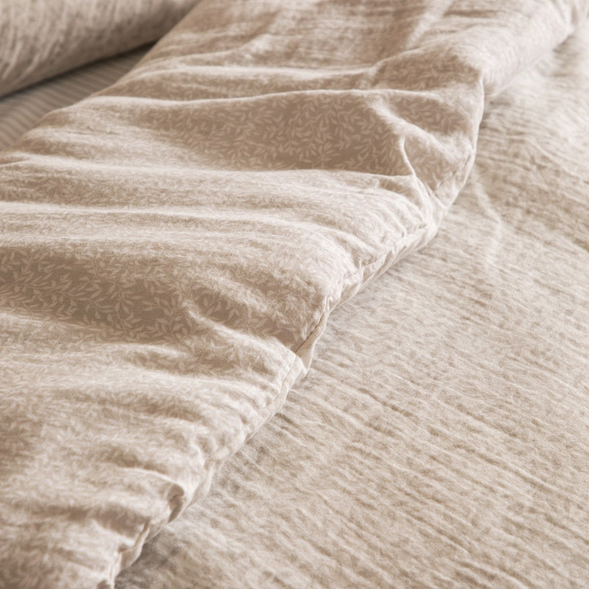 Perrie Leaf Cotton Ditsy Duvet Cover Set in Natural, close-up of crinkled muslin cotton showing the reversible ditsy leaf print folded over a plain textured natural ground.