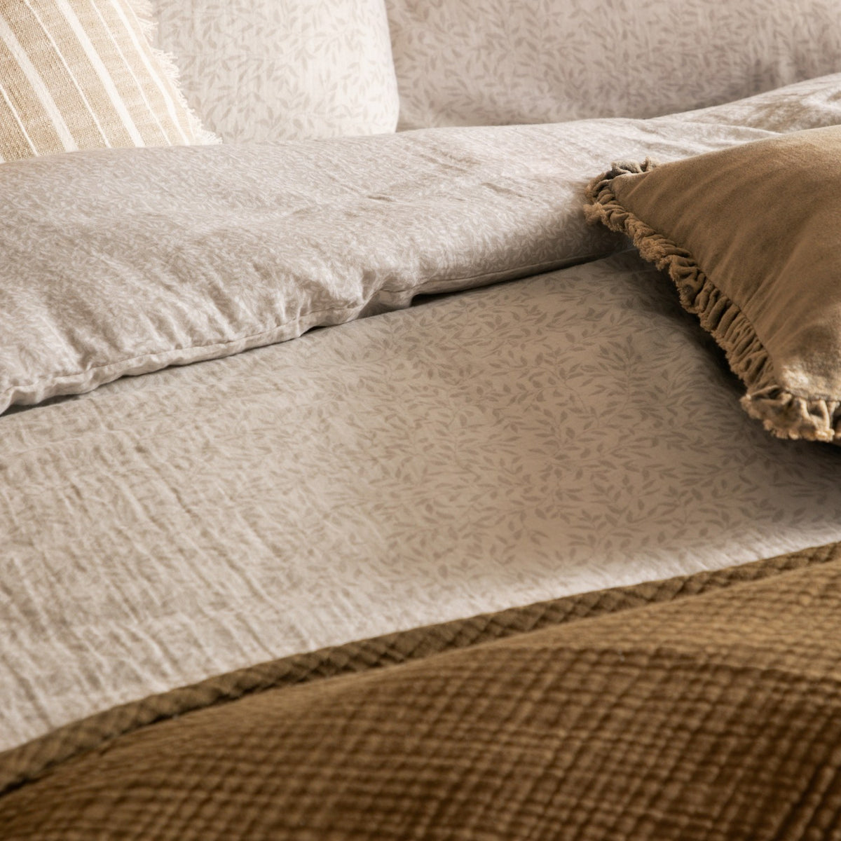 Perrie Leaf Cotton Ditsy Duvet Cover Set in natural tones, close-up on a bed showing the crinkled muslin cotton texture with fringed and velvet cushions.