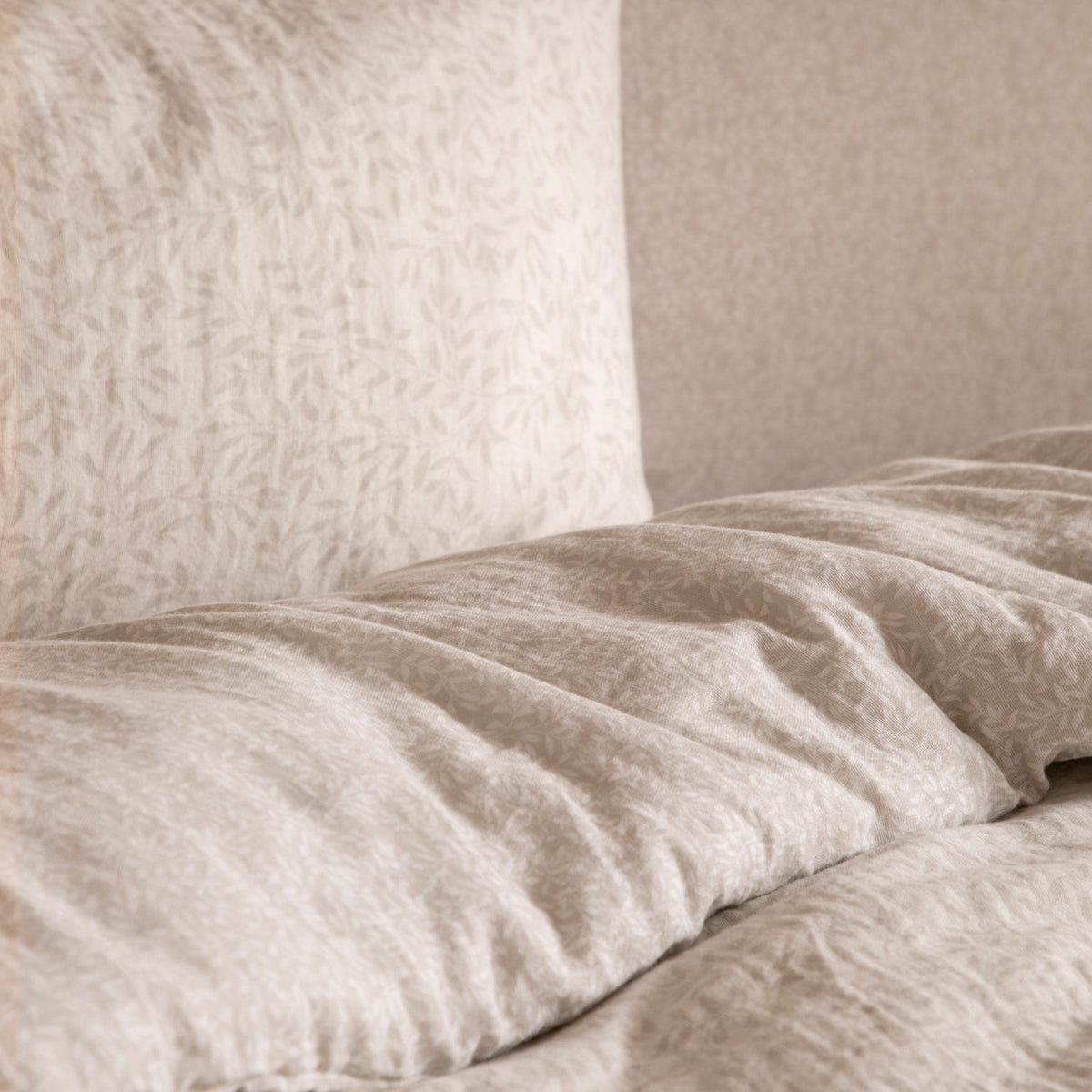 Perrie Leaf Cotton Ditsy Duvet Cover Set in natural, close-up of crinkled muslin cotton bedding with a small leaf print on a pale neutral ground.