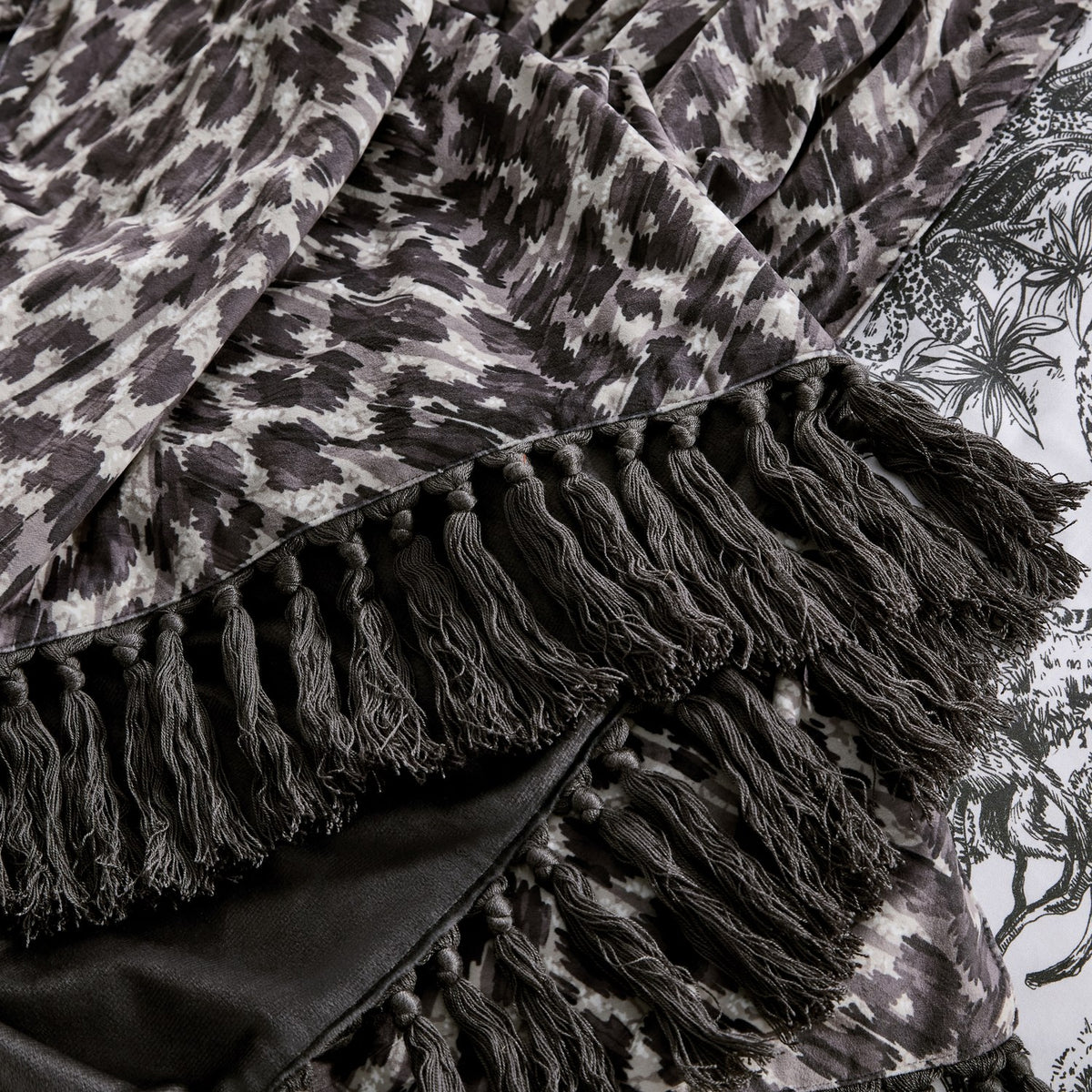 Close-up of the Pokot Animal Velvet Throw in monochrome, showing grey and black leopard-print velvet with a knotted fringe trim edge and plain black reverse side.