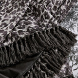 Close-up of the Pokot Animal Velvet Throw in monochrome, showing grey and black leopard-print velvet with a knotted fringe trim edge and plain black reverse side.