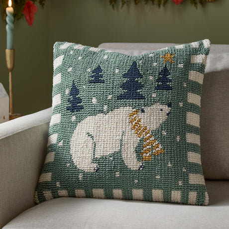 Polar Bear Reversible Cotton Cushion in frosty blue, a 45cm loop-tufted square cushion with a polar bear, navy trees and gold star on green, striped cream border, shown on a sofa.