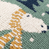 Close-up of the Polar Bear Reversible Cotton Cushion in Frosty Blue, showing loop-tufted cream fur, an amber-gold striped scarf, and a soft green background with navy tree details.