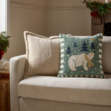 Square 45cm loop-tufted cushion in frosty blue-green with a polar bear, navy trees and gold star design, striped border, shown on a sofa beside a cream textured cushion.