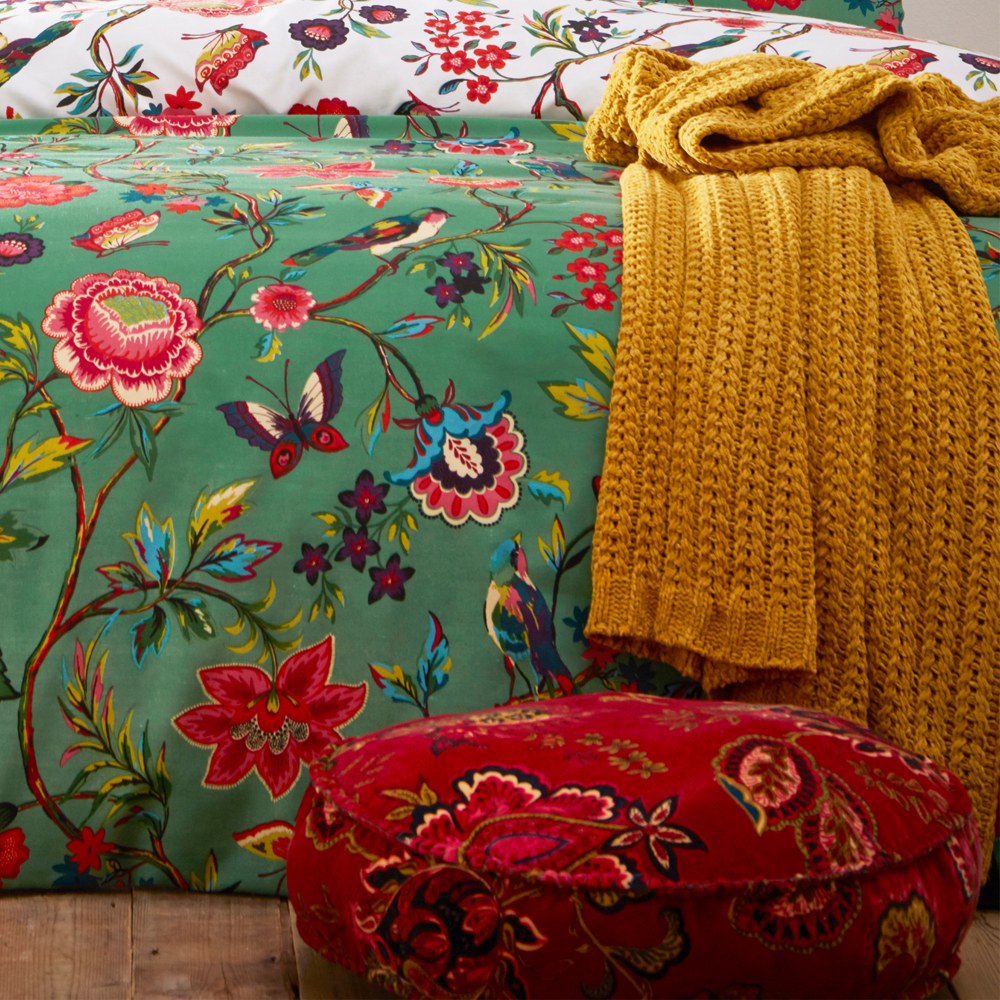 Pomelo Printed Floral Duvet Cover Set in Verdi green on a bed, with a mustard knit throw and red floral round cushion styled alongside on a wooden bench.