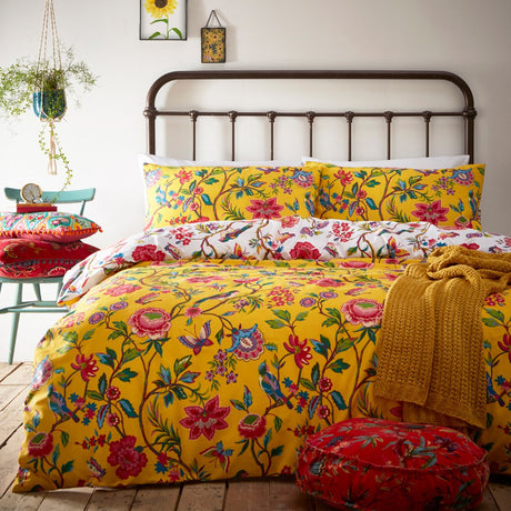 Pomelo Printed Floral Duvet Cover Set in yellow on a bedstead, showing red, pink, blue and green blooms, birds and butterflies, styled in a bedroom with mustard throw and cushions.