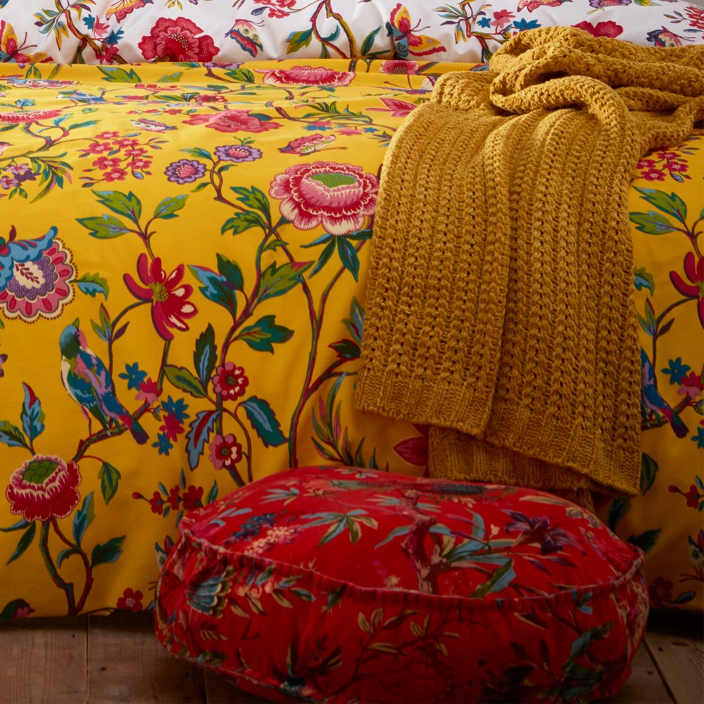 Pomelo Printed Floral Duvet Cover Set in yellow with red, pink, blue and green blooms and birds, styled with a mustard knit throw and red patterned floor cushion.