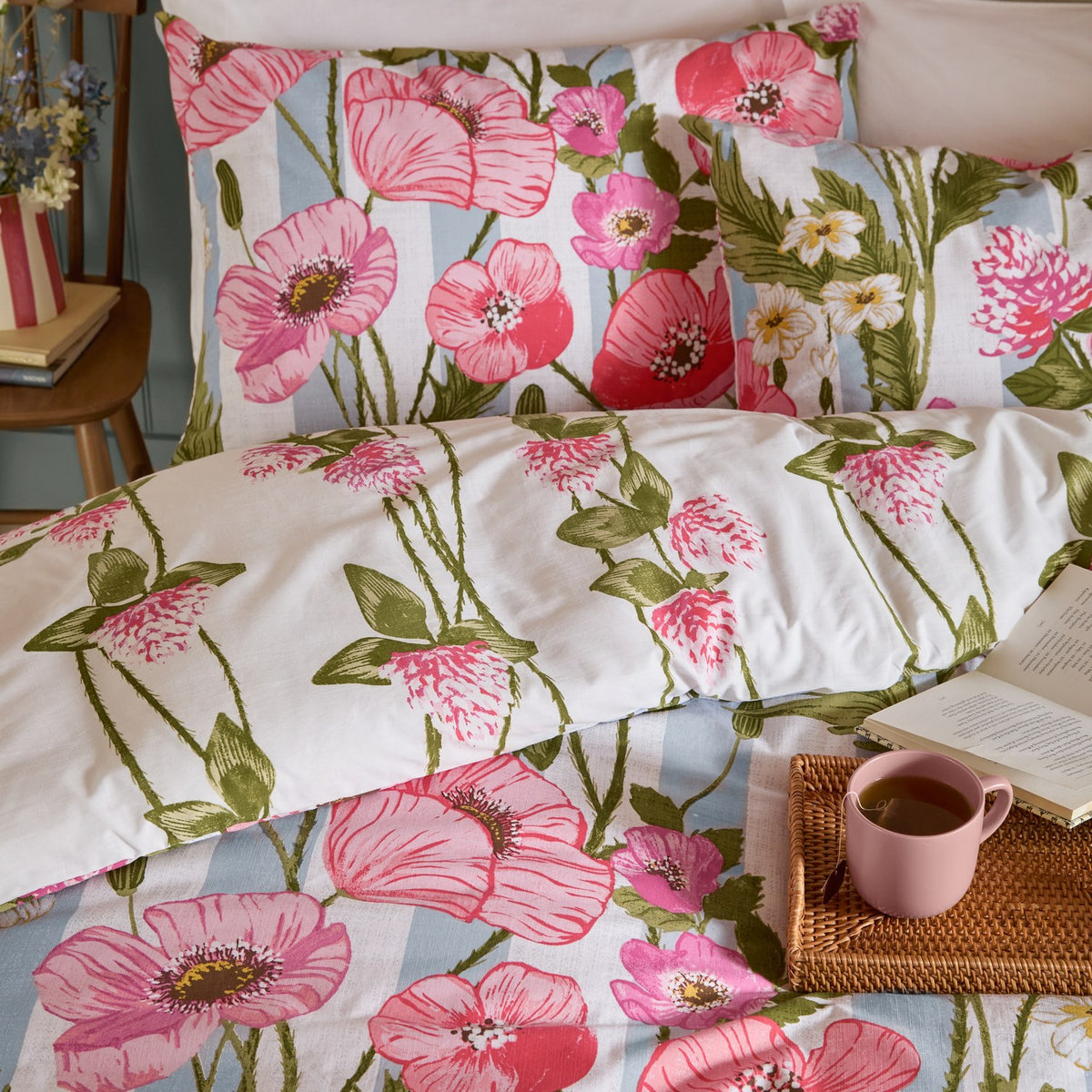 Poppy Trail reversible floral duvet cover set in pink, coral and green, shown styled on a bed with matching pillowcases in a bedroom setting.