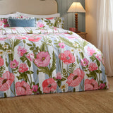 Poppy Trail Reversible Floral Duvet Cover Set in Multi on a bed, showing pink and coral poppies with green foliage on a striped ground, styled in a bedroom with a blue lamp on a bedside table.