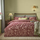 Posie Reversible Floral Duvet Cover Set in Berry on a bed with frilled edges, pink floral pattern, striped reverse, and gingham pillowcases in a bedroom setting.
