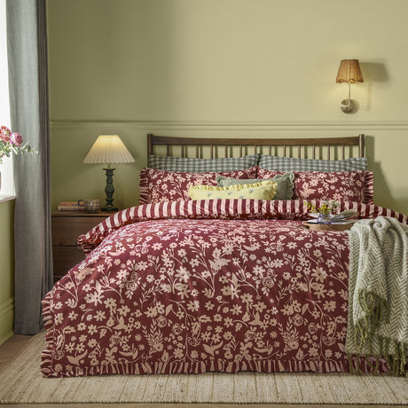 Posie Reversible Floral Duvet Cover Set in Berry on a bed with frilled edges, pink floral pattern, striped reverse, and gingham pillowcases in a bedroom setting.