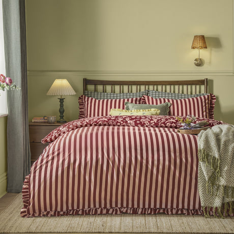 Posie Reversible Floral Duvet Cover Set in Berry, striped side shown on a bed with floral-print pillowcases and frilled edging in a bedroom setting.