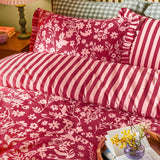 Posie Reversible Floral Duvet Cover Set in Berry, shown on a bed with pink floral pattern on one side and berry-pink stripes on the other, edged with a frilled trim.