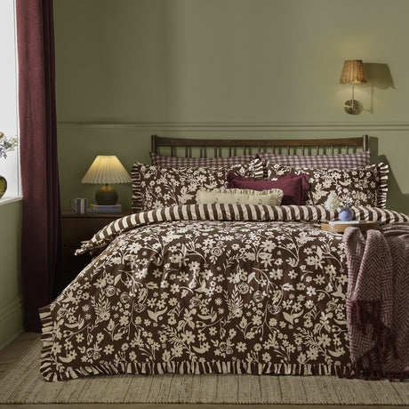 Posie Reversible Floral Duvet Cover Set in chocolate brown, shown on a bed with cream floral print, striped reverse side, and frilled edge trim, styled in a green-walled bedroom.