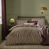 Posie Reversible Floral Duvet Cover Set in chocolate showing the striped side with frilled trim, styled on a bed with floral cushions in a green bedroom.