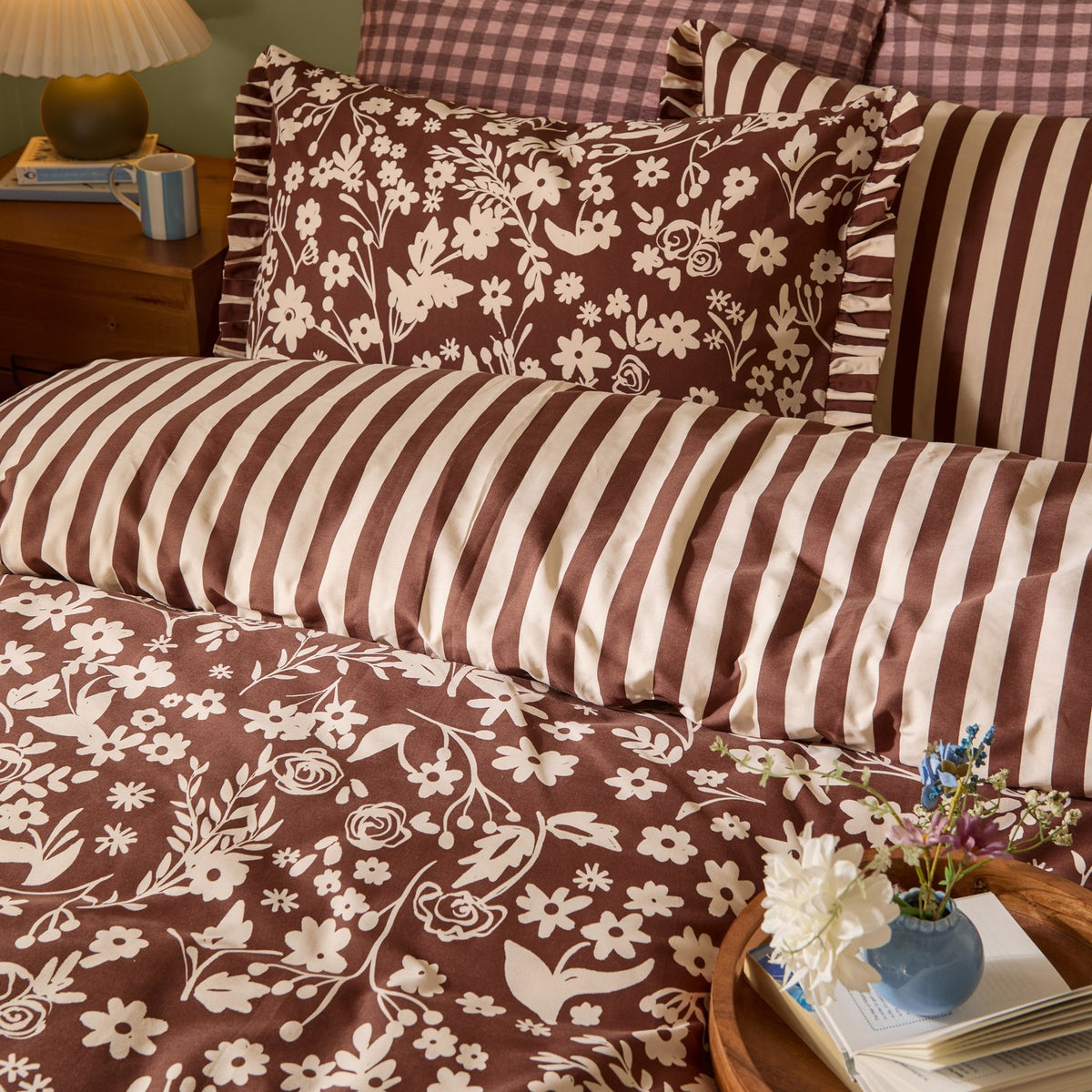 Posie Reversible Floral Duvet Cover Set in Chocolate, showing cream floral print and reverse chocolate-and-cream stripe with frilled-edge pillowcases, styled on a bedroom bed.
