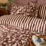 Posie Reversible Floral Duvet Cover Set in Chocolate, showing cream floral print and reverse chocolate-and-cream stripe with frilled-edge pillowcases, styled on a bedroom bed.