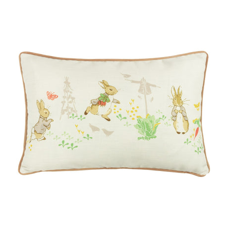 Rectangular cream cushion from the Peter Rabbit Classic range with tan piping, printed with rabbit illustrations, carrots, cabbages, a scarecrow and butterfly, shown on a white background.