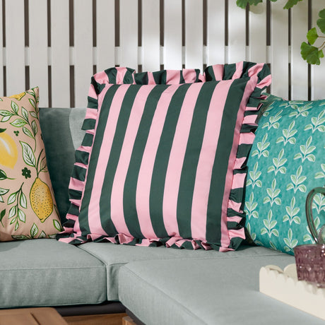 Palm Royale Stripe cushion in deep green and pink polyester with a ruffle trim edge, shown on a sofa alongside patterned cushions in an outdoor living setting.