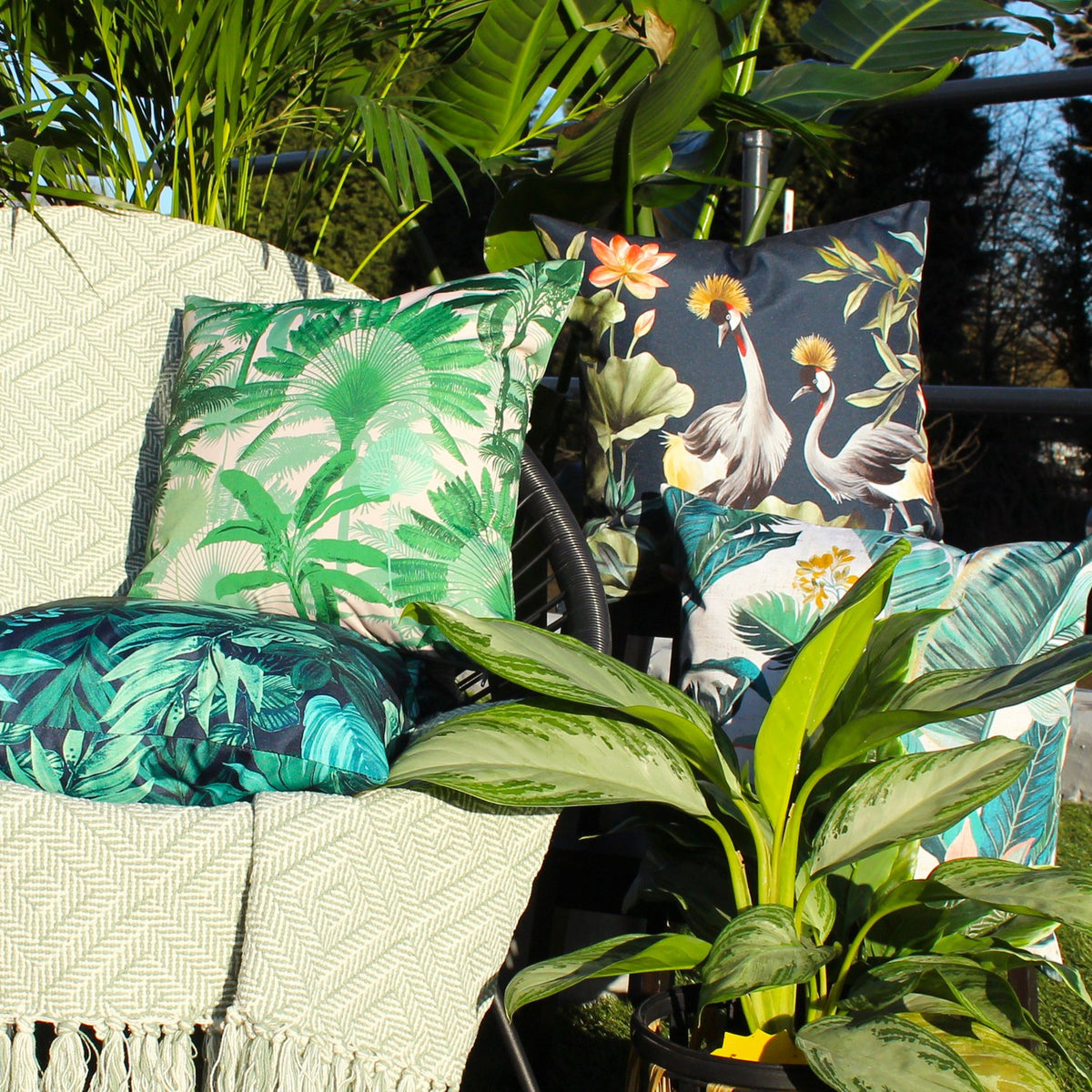 Psychedelic Jungle Reversible Polyester Cushion in green, square with dense tropical leaf print in deep green and blue-green tones, styled on a garden chair among cushions and foliage.