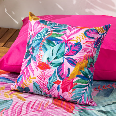 Psychedelic Jungle Reversible Polyester Cushion in Multi, a square outdoor cushion with a dense tropical leaf print in pink, teal, blue, green and gold, shown on a bright pink outdoor seat cushion.