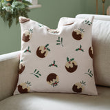 Square cream velvet cushion with tufted Christmas pudding motifs in brown and cream, accented by embroidered holly, mistletoe, and red berries, shown on a sofa.